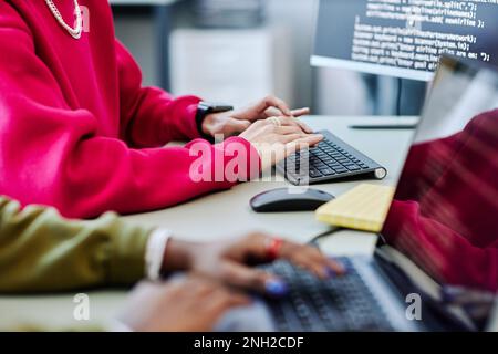 Close up of young person typing at computer keyboard while writing code in software development office, magenta accent Stock Photo