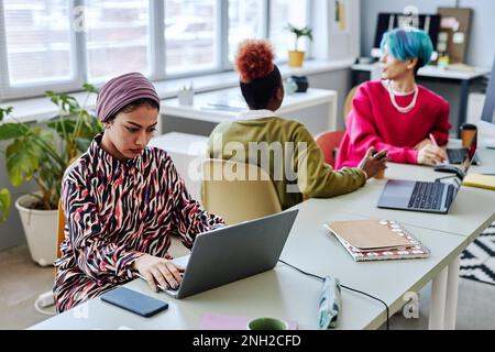 Diverse team of software developers working in office focus on Muslim young woman using computer in foreground, copy space Stock Photo