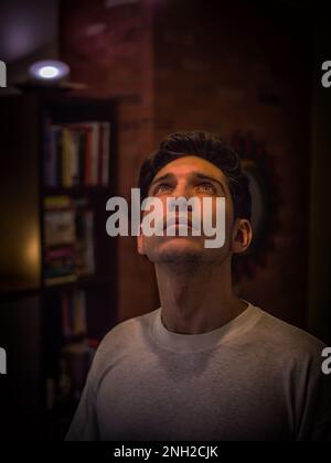 Young man standing near bookcase and looking up Stock Photo