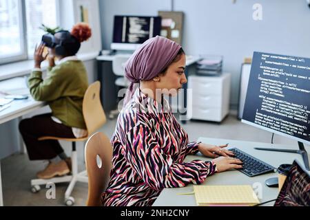 Side view portrait of Muslim young woman as software developer writing code and using computer in office Stock Photo