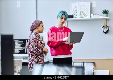 Waist up portrait of two gen Z young people using laptop white standing in office, focus on Asian man with colored hair Stock Photo