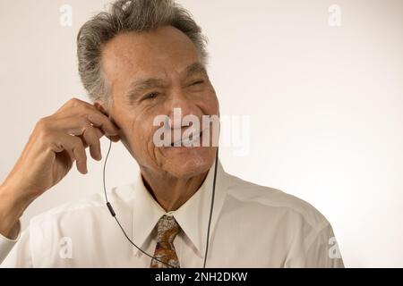 Older man listening to music or a podcast using ear buds on his smartphone Stock Photo