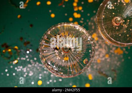 Two exquisite glasses of champagne with silver glitters and confetti. Stylish alcohol cocktail on green background with gold serpentine and glitters. Stock Photo