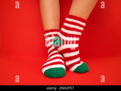 Female feet in fluffy New Year or Christmas warm socks. The colors of the socks are red and white stripes and green heels and tips. Girls legs on a re Stock Photo