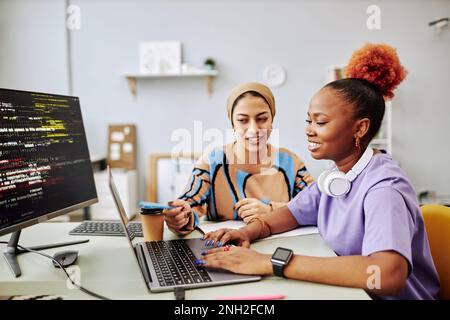 Side view portrait of two young women working on software development project together and smiling happily Stock Photo