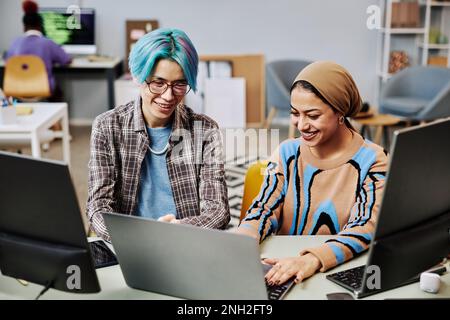 Portrait of two young software developers using computers in office and smiling happily enjoying work Stock Photo