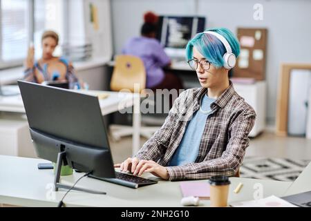 Portrait of young man with blue hair using computer in office and wearing headphones Stock Photo