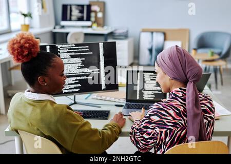 Back view at two female programmers writing code and discussing project together Stock Photo