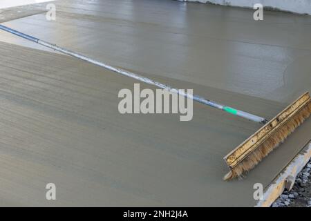 Construction workers use broom to brush freshly wet concrete on surface resulting in formation of groove texture patterns Stock Photo