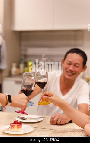 Asian man having a celebration with friends toasting glass of red at dinner party. Stock Photo