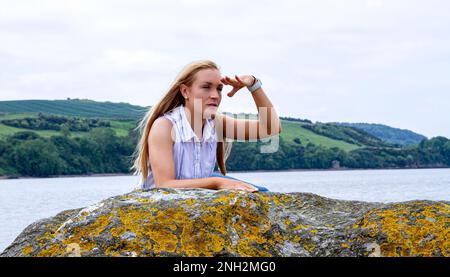 On a beautiful October day in Wormit Beach, Fife, Rhianna Martin sits on large rocks beside the River Tay, Scotland Stock Photo