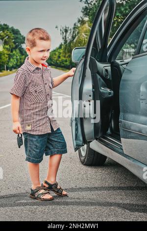 Chernihiv, Ukraine - August 15, 2014: A little boy opens a car. A little boy is holding car keys in his hand. Little boss. Stock Photo