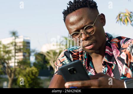 use technology as a tool to organize your business, portrait of concentrated young african ethnicity man working using his phone in sitting outdoors Stock Photo