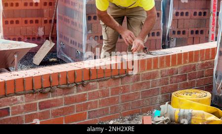 Industrial bricklayer laying bricks on cement mix on construction site Stock Photo