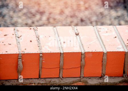 Close up of a brick wall and jointer trowel used by the worker to apply and level the mortar between bricks. Bricklayer making finishing touches to th Stock Photo