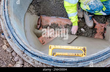 A builder in the new built manhole benching it with sand and cement mix. Concept of repairing underground utilities and services Stock Photo