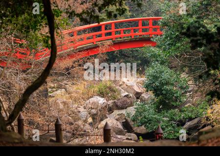 Arched red bridge over dry rocky river in quiet forest Stock Photo