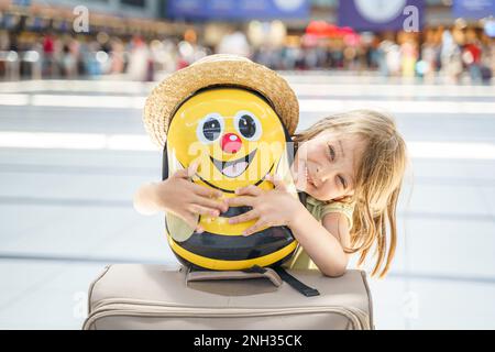 Girl with big funny suitcase, bag in airport terminal. Waiting for boarding to flight. Happy family vacation travel.Luggage baggage check in departure Stock Photo