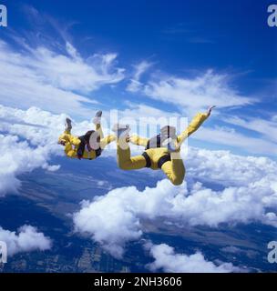 To skydivers freefalling while holding hands above the clouds Stock Photo