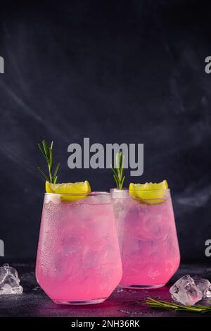 Refreshing pink drink or cocktail with ice, garnished with a slice of lime and rosemary. Stock Photo