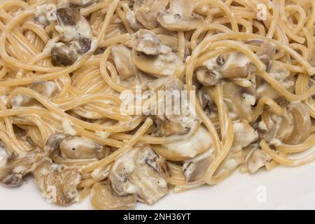 Close-up of a large plate of juicy spaghetti with mushrooms, garnished with fresh herbs on top. Italian cuisine and gourmet food concept. Stock Photo