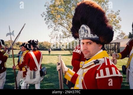 A Red Coat (British) soldier stands in front of flags in a camp during ...