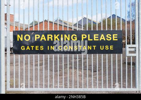 Large yellow and black sign on metal gate saying no parking please gates in constant use Stock Photo