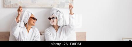 happy interracial women in white towels and stylish sunglasses toasting with champagne and looking at each other, banner,stock image Stock Photo