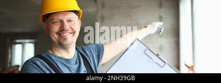 Smiling builder worker in hard hat holding blank sheet of paper on clipboard Stock Photo