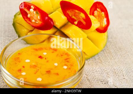 Closeup of red chili pepper rings, cutted half of mango and mango chili jam on rustic style sackcloth. Soft focus Stock Photo