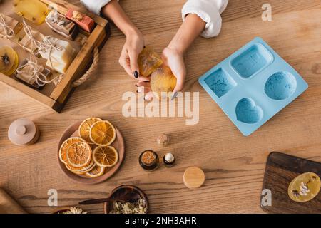 top view of cropped african american woman holding herbal soap near natural ingredients and silicone mold on wooden table,stock image Stock Photo