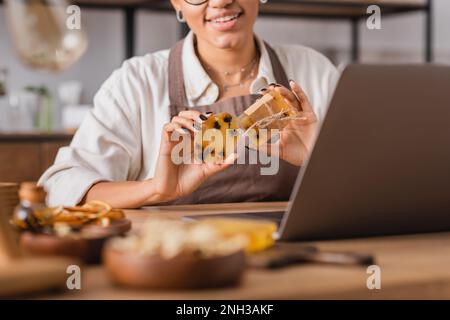 cropped view of smiling african american craftswoman showing herbal soap while having video call on laptop,stock image Stock Photo