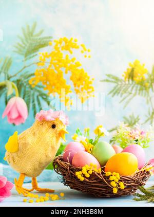 Easter decoration with funny chick, spring flowers and colorful dyed eggs in nest Stock Photo