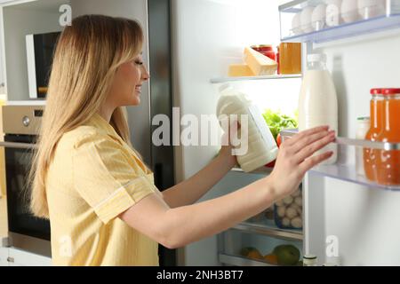 Young woman putting gallon of milk into refrigerator in kitchen Stock Photo