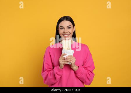 Happy young woman with delicious shawarma on yellow background