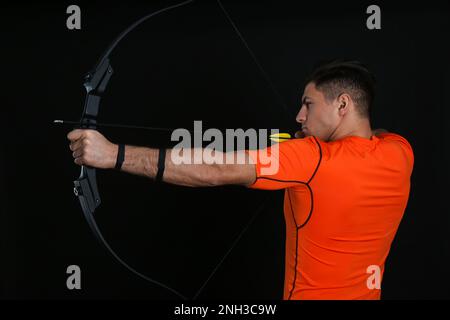 Man with bow and arrow practicing archery on black background Stock Photo