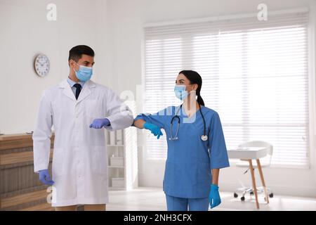 Doctors with protective masks greeting each other by bumping elbows instead of handshake in clinic Stock Photo