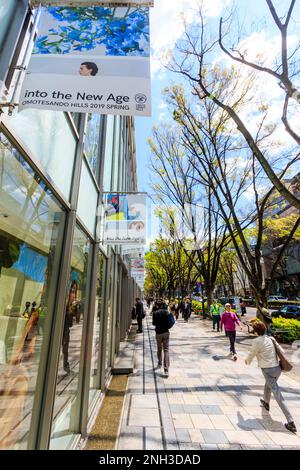 View along exterior of the Omotesando Hills shopping complex in Central Tokyo. Some people walking along street on a springtime day. Blue sky. Stock Photo