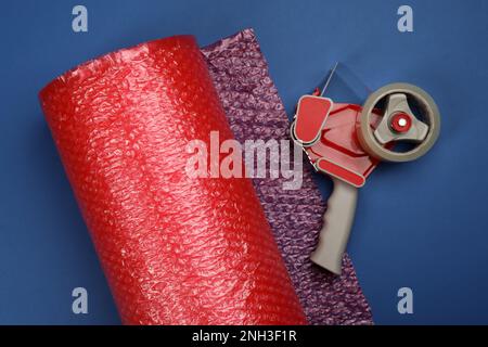 Bubble wrap roll and tape dispenser on blue background, flat lay Stock Photo