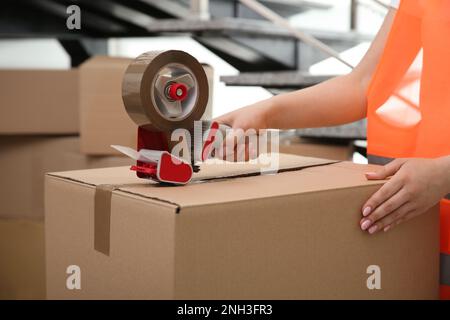 Worker taping cardboard box indoors, closeup view Stock Photo