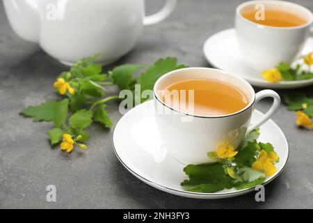 Cup of aromatic celandine tea and flowers on grey table Stock Photo