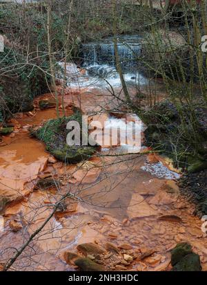polluted river water rocks stained orange from chemicals released up stream Stock Photo