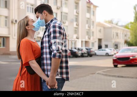 Couple in medical masks trying to kiss on light blue background Stock ...