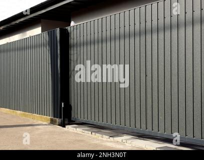gray metal fence and gate with vertical panels and grooves. powder coat finish. diminishing perspective view. corrugated pressed steel sheet material Stock Photo