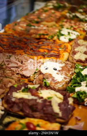 Various flavors pizza cut into square slices on display, in a restaurant. Stock Photo