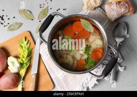 Pot of delicious vegetable bouillon and ingredients on light grey table, flat lay Stock Photo