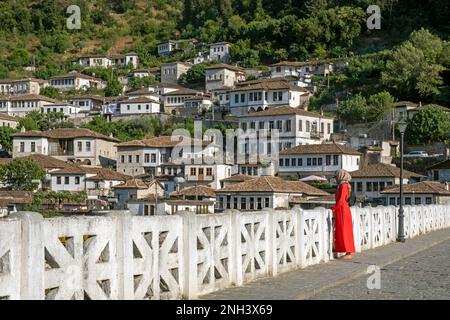 Albanian Muslim woman / muslima wearing red dress and hijab / headscarf on the Gorica Bridge over the Osum river in the city Berat / Berati, Albania Stock Photo