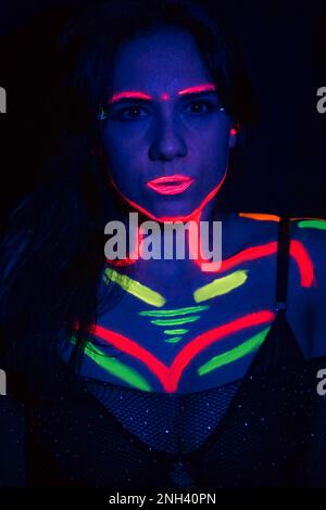 Fashion model woman in neon light, portrait of a beautiful model with fluorescent makeup, body art design in UV, painted face, colorful makeup, on a b Stock Photo