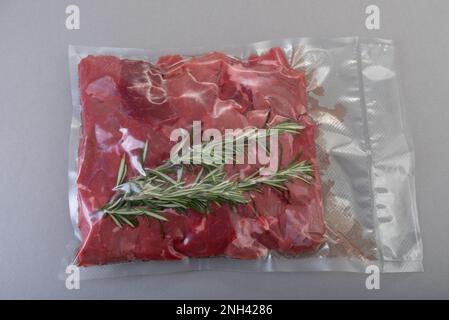 Raw beef diced for stew with rosemary sprig in vacuum-sealed package for sous vide cooking on gray background Stock Photo
