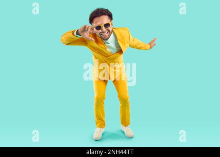Cool funny man showing v-sign and looking at you through it on light blue background in studio. Stock Photo